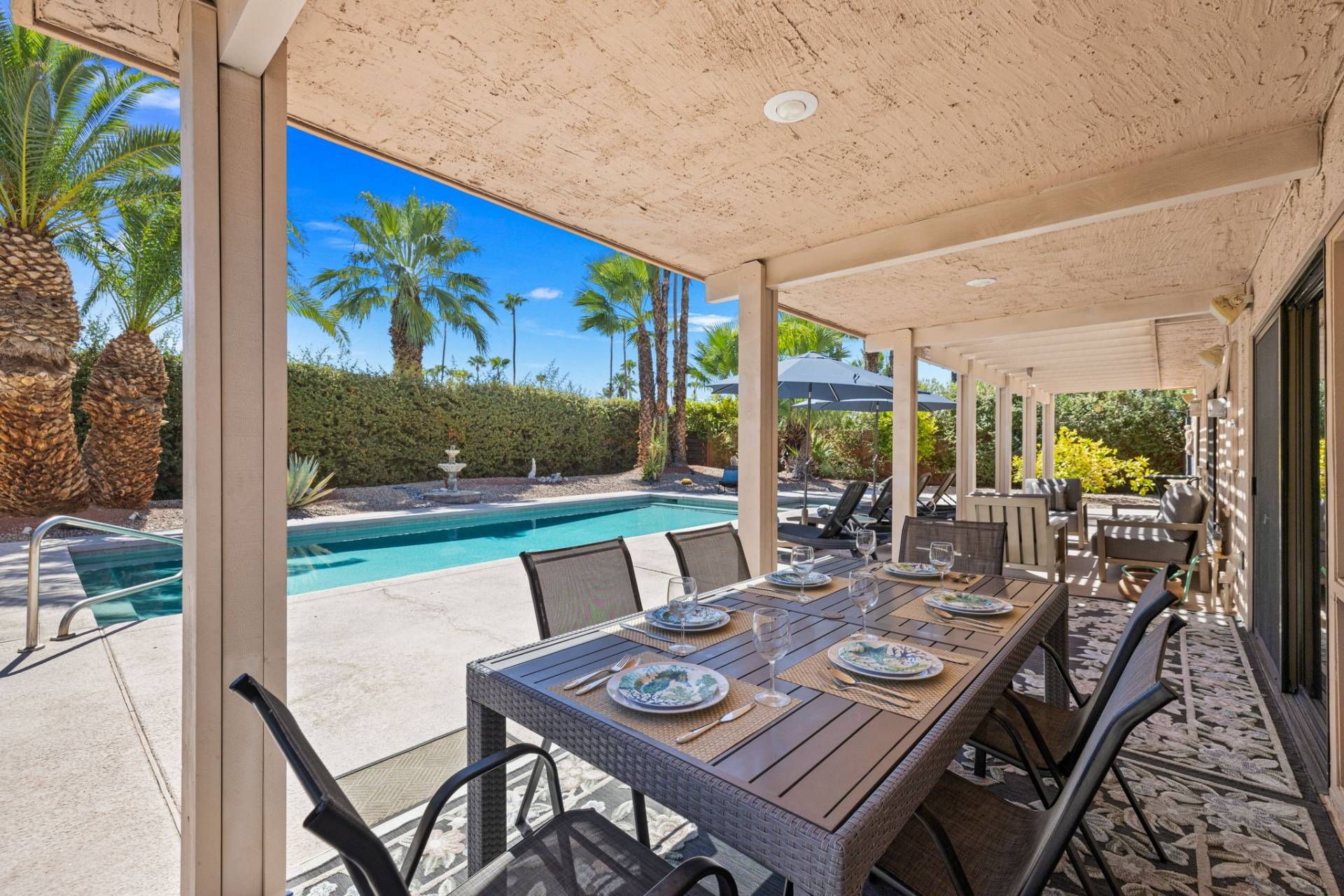Een terras met een zwembad, palmbomen en een pergola.