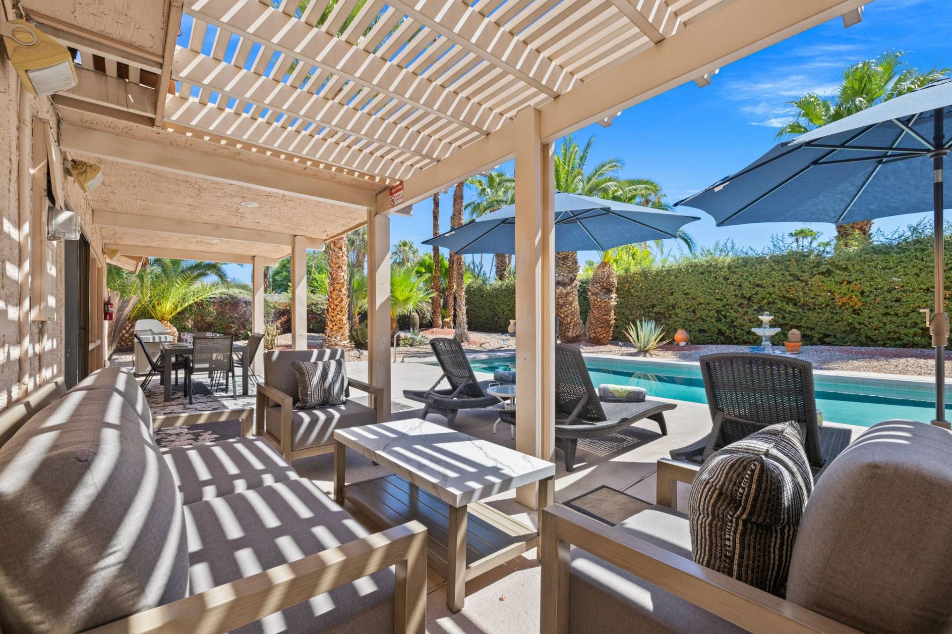 A covered outdoor seating area with tables and chairs, overlooking a swimming pool.