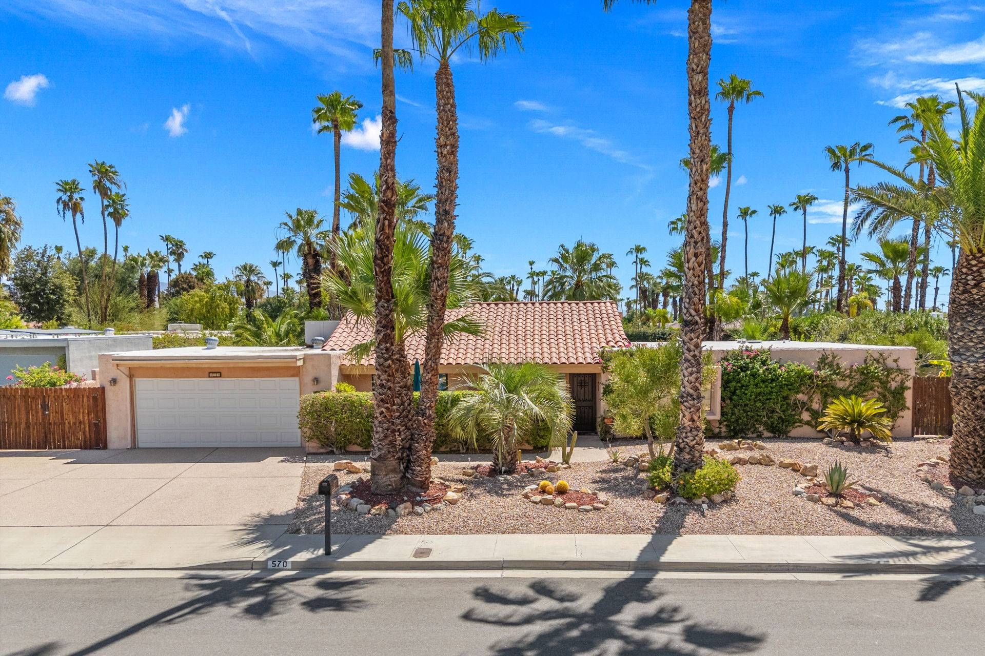 A residential area with a house featuring a tiled roof, surrounded by palm trees and a well-maintained garden.