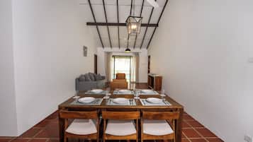 Un comedor con una larga mesa de madera dispuesta para seis personas, flanqueada por sillas de madera con cojines blancos.