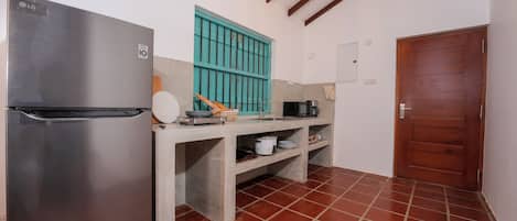 A compact kitchen with a stainless steel refrigerator, a teal-colored window, and a wooden door.