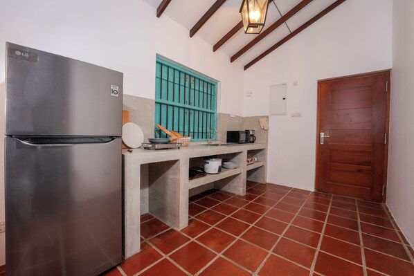 A compact kitchen with a stainless steel refrigerator, a teal-colored window, and a wooden door.