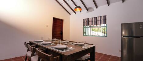 Un comedor con una mesa de madera dispuesta para cuatro, un ventilador de techo, una ventana con vistas y un refrigerador.