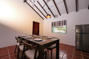 A dining area with a wooden table set for four, a ceiling fan, a window with a view, and a refrigerator.