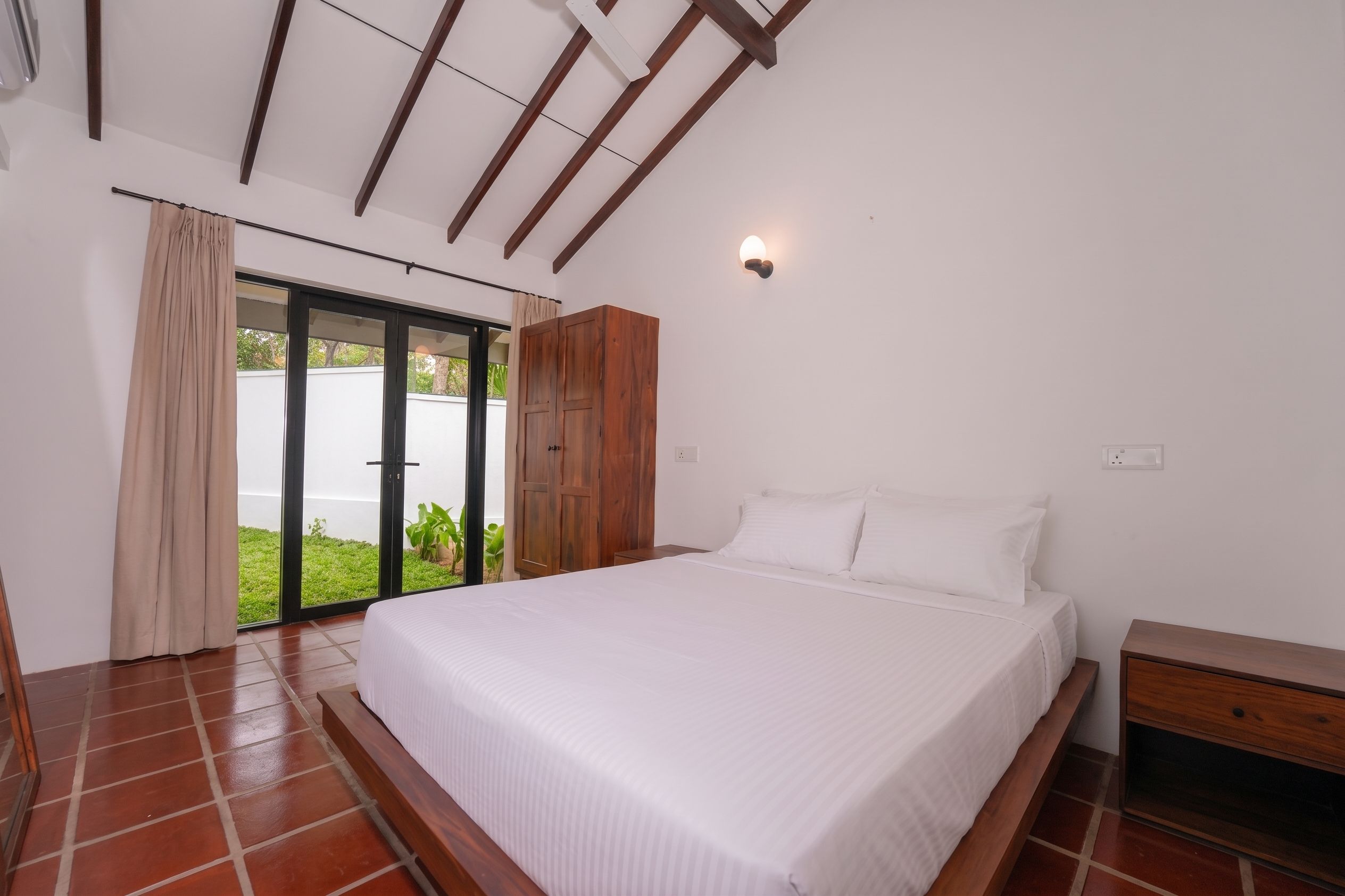 A bedroom with a bed, wooden wardrobe, and a sliding glass door leading to a balcony.