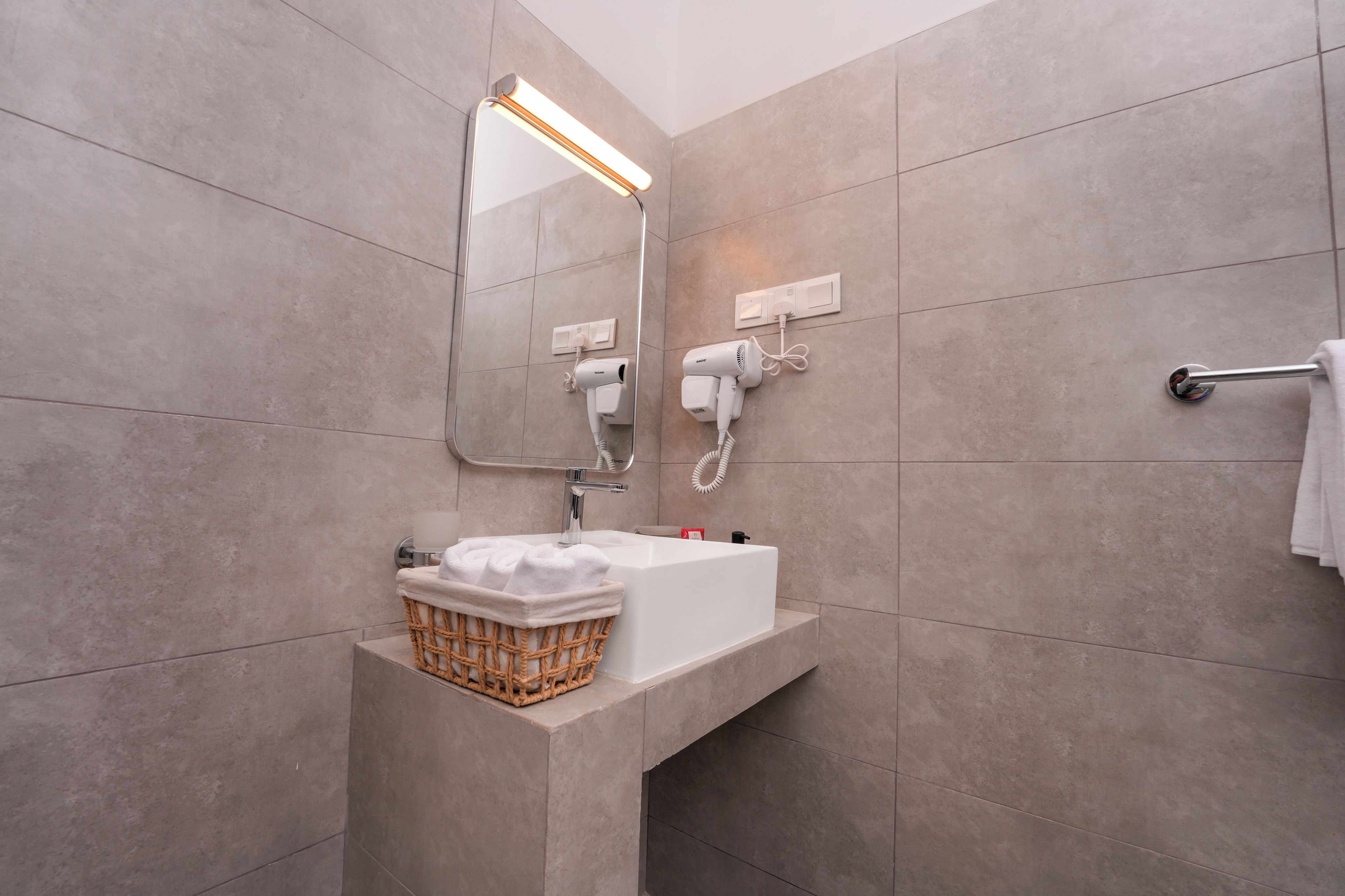 A modern bathroom with a white sink, a mirror, a hairdryer, and a towel rack.