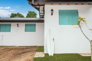 A building with a white exterior, green shutters, and a surfboard leaning against the wall.