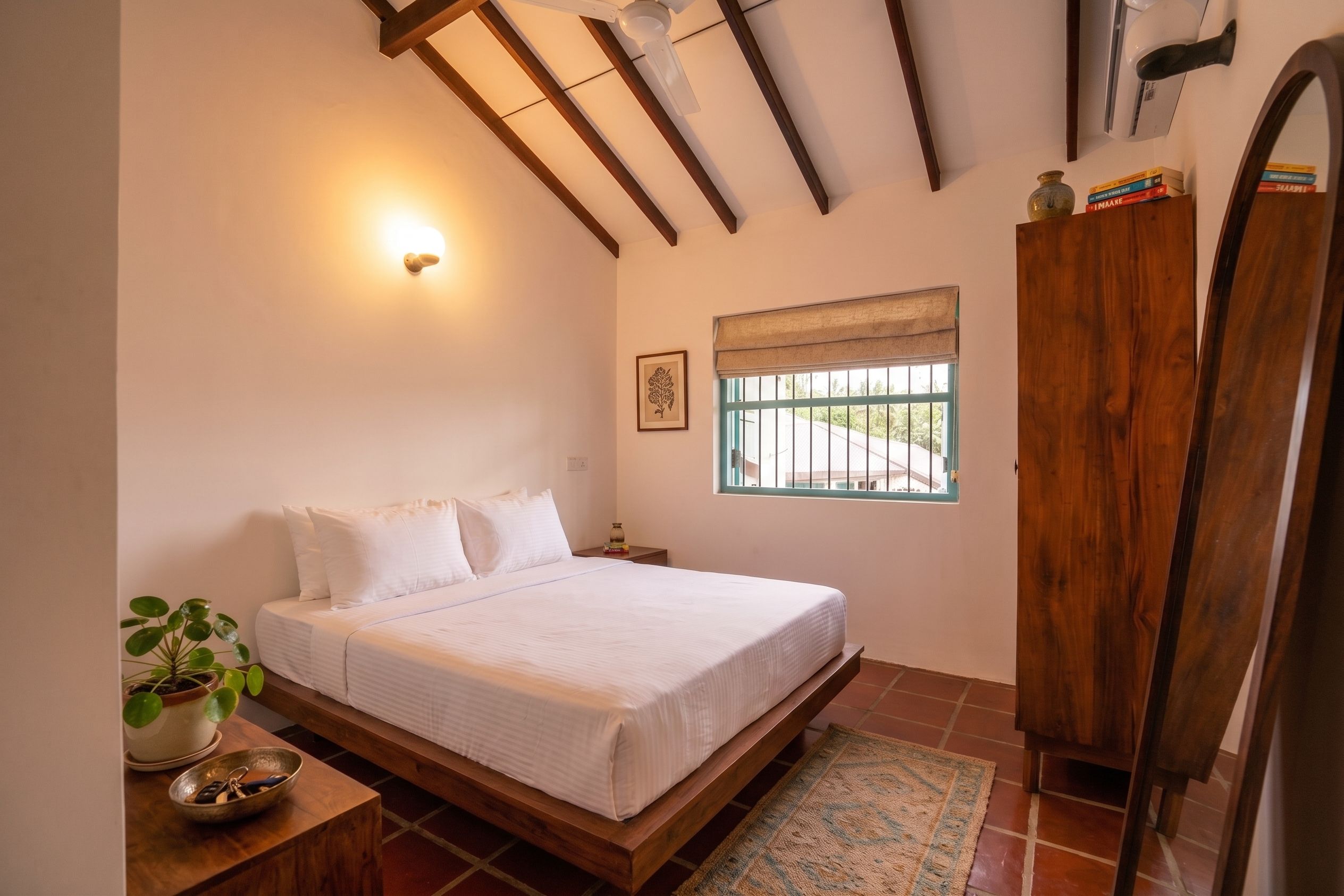 Un dormitorio con cama, mesita de noche, planta en maceta, ventana con vistas y armario de madera.