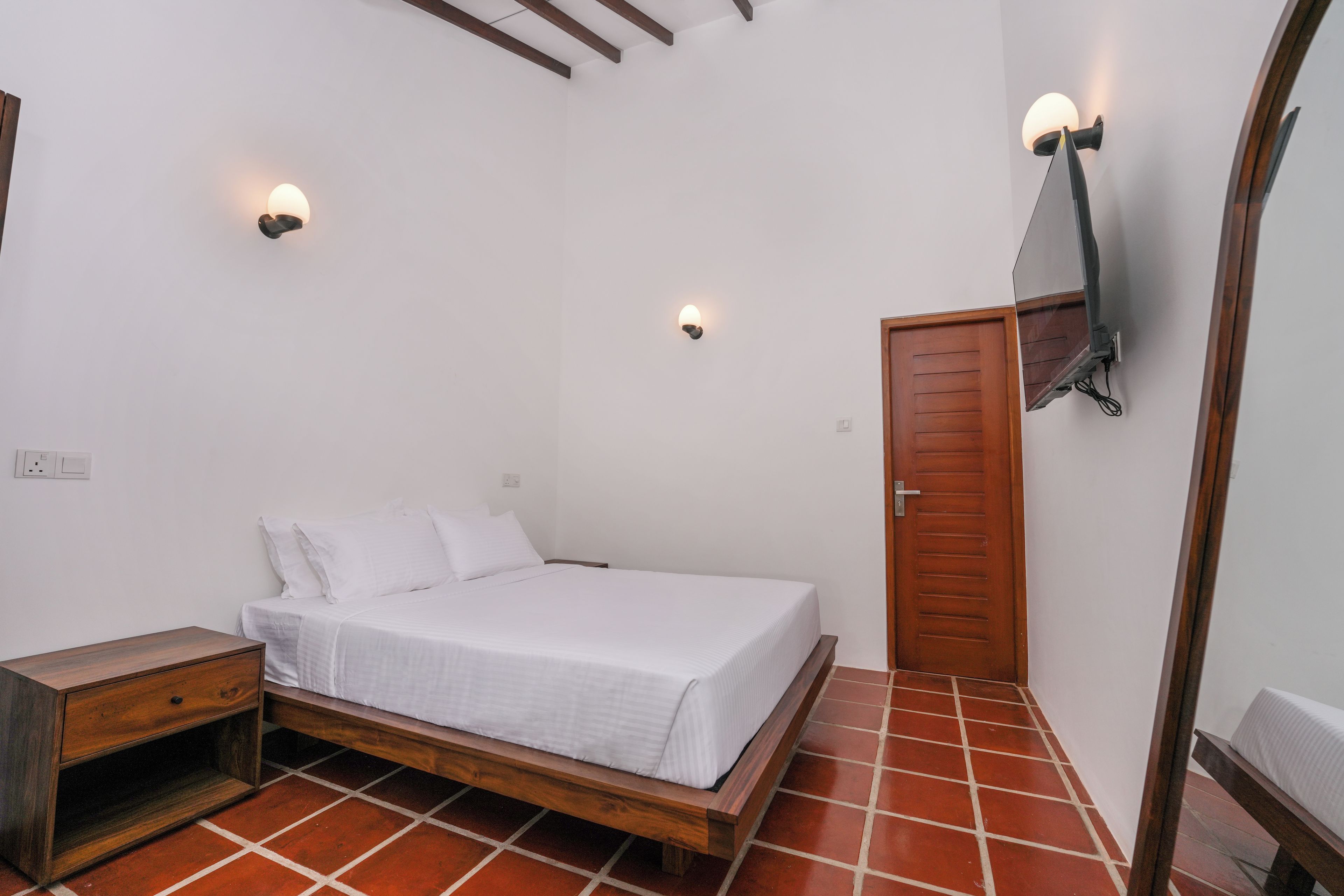 A bedroom with a wooden bed, white bedding, a wooden nightstand, and two wall-mounted lights.