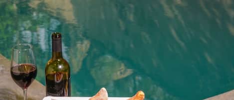 A poolside setting with a basket of bread, a bottle of wine, and a plate of grapes.