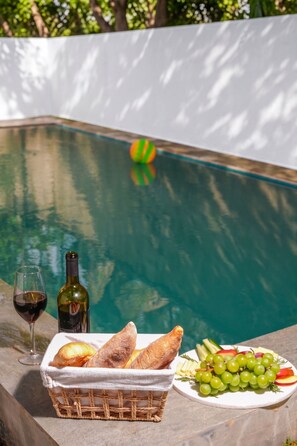 A poolside setting with a basket of bread, a bottle of wine, and a plate of grapes.