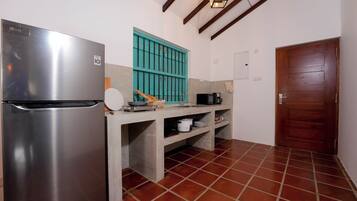 Cocina compacta con refrigerador de acero inoxidable, ventana color turquesa, microondas y puerta de madera.