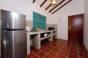 A compact kitchen with a stainless steel refrigerator, a teal window, a microwave, and a wooden door.