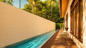 En swimmingpool som ligger intill en byggnad med en vit yttervägg och träfönsterkarmar.