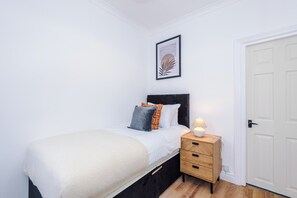 Ein Schlafzimmer mit einem Bett, einem Nachttisch mit Lampe, einer Tür und einem gerahmten Bild an der Wand.