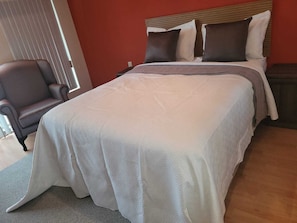 Ein Schlafzimmer mit einem Bett, einem Sessel und einem Fenster mit Jalousien.
