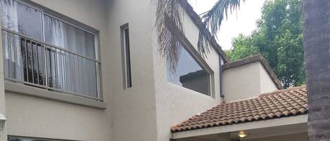 A two-story building with a tiled roof, a balcony, and a garden area with various plants and flowers.