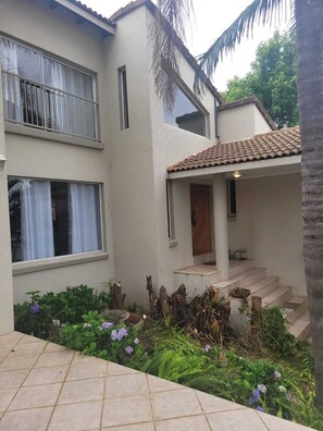 Ein zweistöckiges Gebäude mit Ziegeldach, einem Balkon und einem Garten mit verschiedenen Pflanzen und Blumen.