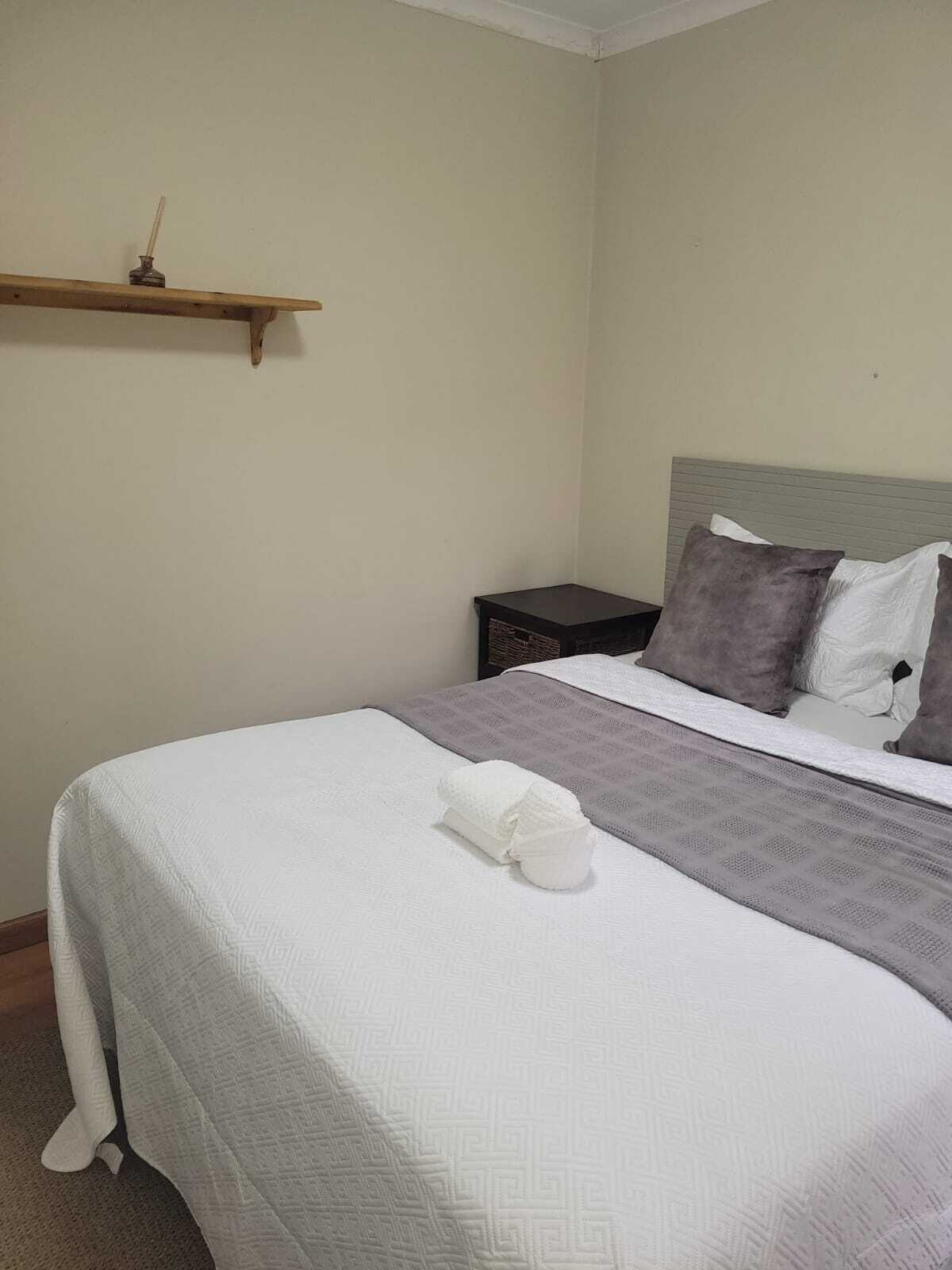 Ein ordentlich bezogenes Bett mit einer weißen Daunendecke, einem gefalteten Handtuch, einer grauen Tagesdecke und zwei Kissen.