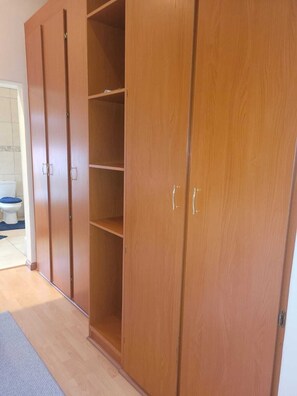 A wooden wardrobe with multiple doors and shelves, a toilet visible in the background, and a blue mat on the floor.