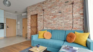 Ein Wohnzimmer mit blauem Sofa, Holztisch und Backsteinwand.