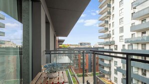Ein Balkon mit Tisch und Blumentöpfen, der auf einen Innenhof mit einem Gebäude im Hintergrund blickt.