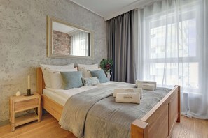 Ein Hotelzimmer mit einem großen Bett, einem Nachttisch, einem Spiegel, einem Fenster mit Vorhängen und einer Ziegelwand.
