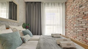 Ein Hotelzimmer mit einem großen Bett, einem Spiegel, einer Ziegelwand und einem Fenster mit Vorhängen.