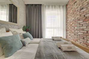 A hotel room with a large bed, a mirror, a brick wall, and a window with curtains. - Bastion Wałowa 49 | City Center | Parking (Gdańsk)