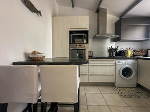Eine kompakte Küche mit Mikrowelle, Backofen, Toaster und Waschmaschine. Ein Esstisch mit Stühlen und ein Korb Brot stehen auf der Arbeitsfläche.