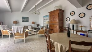 Een ruime woonkamer met een hoge plafond, een kroonluchter en een eethoek met een tafel en stoelen.