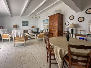 Ein geräumiges Wohnzimmer mit hohen Decken, einer Chandelüster und einem Essbereich mit Tisch und Stühlen.