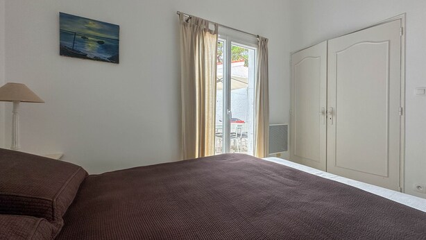 Een slaapkamer met een bed, een kledingkast, een schilderij en een raam met gordijnen.