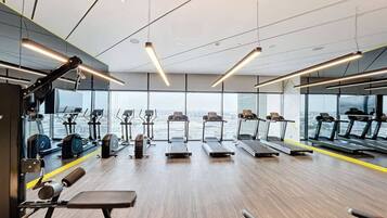 A gym with treadmills, exercise equipment, and large windows offering a city view.