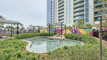 A swimming pool with a tiled deck, surrounded by greenery and a colorful mural.