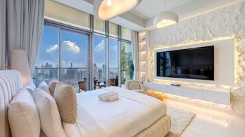 A modern hotel room with a large bed, a flat-screen TV mounted on a textured wall, and a city view through large windows.