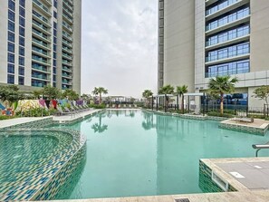 A swimming pool with a tiled edge, surrounded by a fence and palm trees, with high-rise buildings in the background. - Luxurious Studio l Prime Area l City View (Business Bsy)