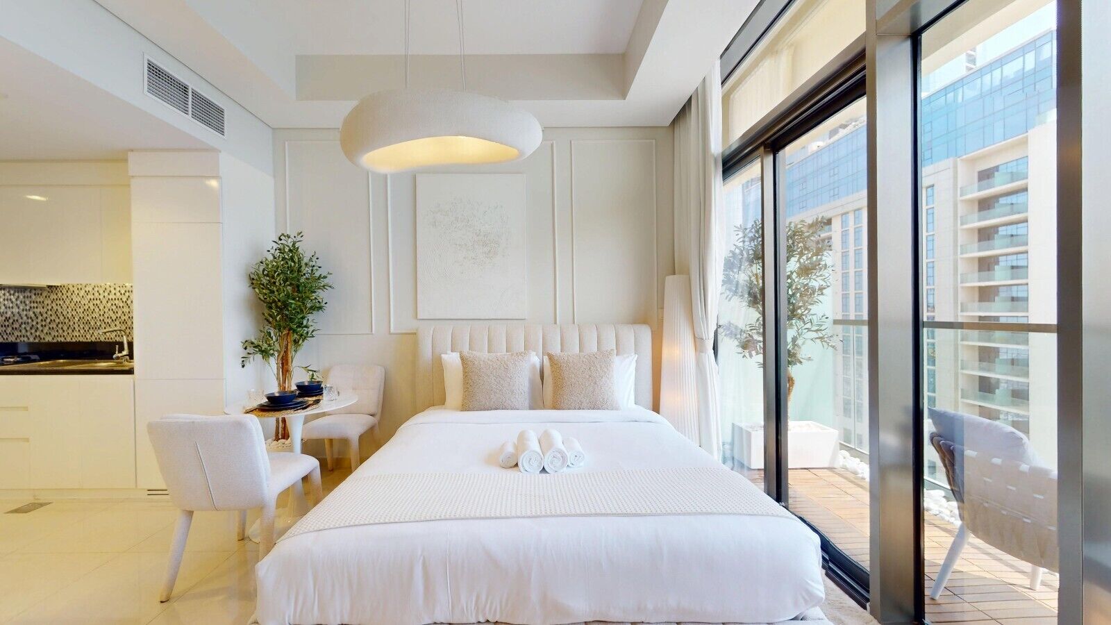 A hotel room with a large bed, a desk, and a view of the city through large windows.