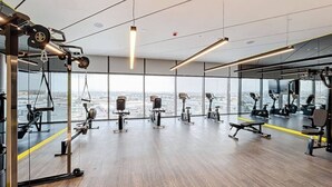 A modern gym with various exercise equipment, large windows, and a view of the cityscape. - Luxe Studio in Prime Area l City View (Business Bsy)