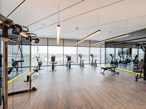 A modern gym with various exercise equipment, large windows, and a view of the cityscape. - Luxe Studio in Prime Area l City View (Business Bsy)
