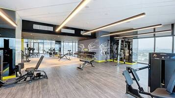 A modern gym with various exercise equipment, large windows, and a high ceiling.