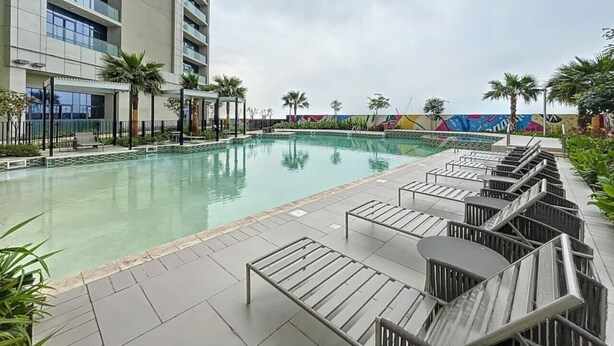 A swimming pool with lounge chairs, a building with balconies, and a colorful mural in the background. - Luxe Studio in Prime Area l City View (Business Bsy)