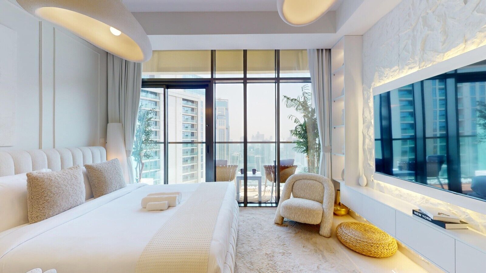 A modern hotel room with a large bed, a sitting area with a chair, and a large window offering a city view.