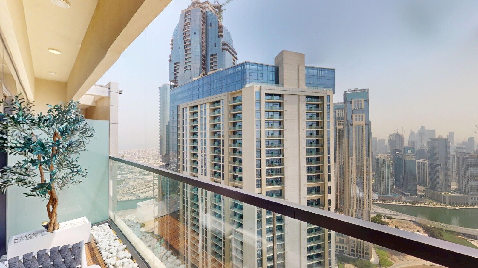A high-rise building with a glass facade, a balcony with a potted plant, and a view of the cityscape.
