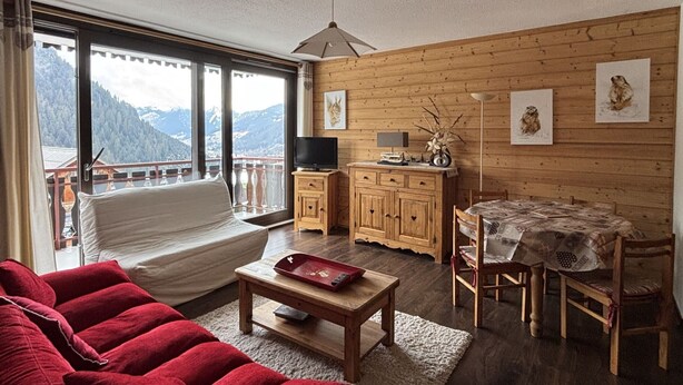 Een gezellige woonkamer met een bank, een houten kast, een eettafel met stoelen en een televisie.
