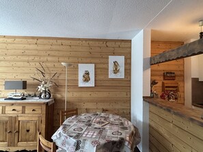Ein Holzinterieur mit einem Esstisch, bedeckt mit einer gemusterten Tischdecke, Holzkredenzen, einer Lampe und zwei an der Wand befestigten Kunstwerken.