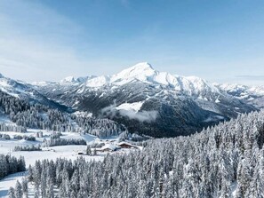 Eine verschneite Berglandschaft mit einer Hütte und bewaldetem Gebiet.