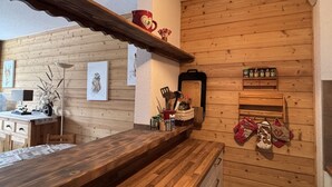 Een houten interieur met een keukenblad, een hanglamp en een plank met keukengerei.