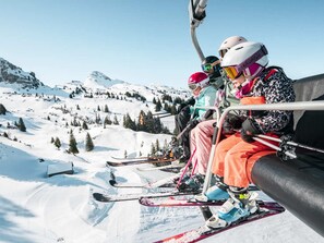 A ski lift with skiers seated, snow-covered slopes, and a mountainous backdrop. - Practical apartment, balcony - 5 guests (Châtel)