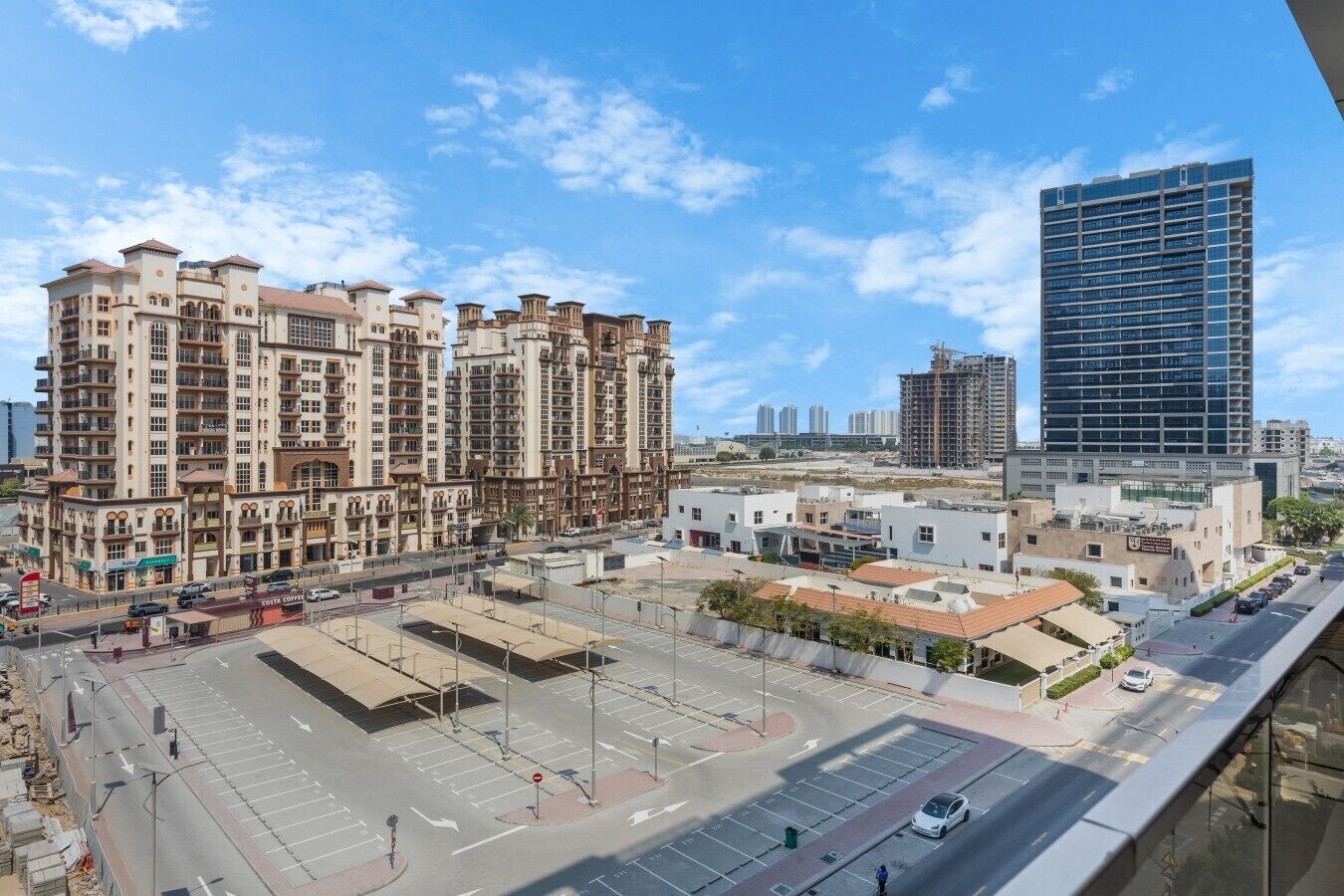 Un edificio residencial de varios pisos con balcones, un estacionamiento y una calle con semáforos.